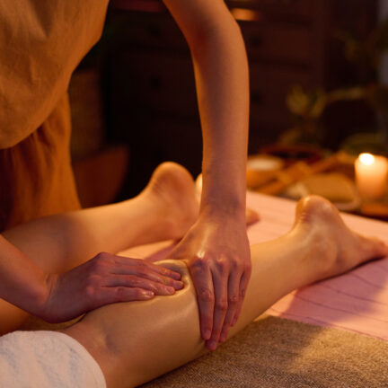 Medium close up of unrecognizable professional spa worker massaging calf of female client